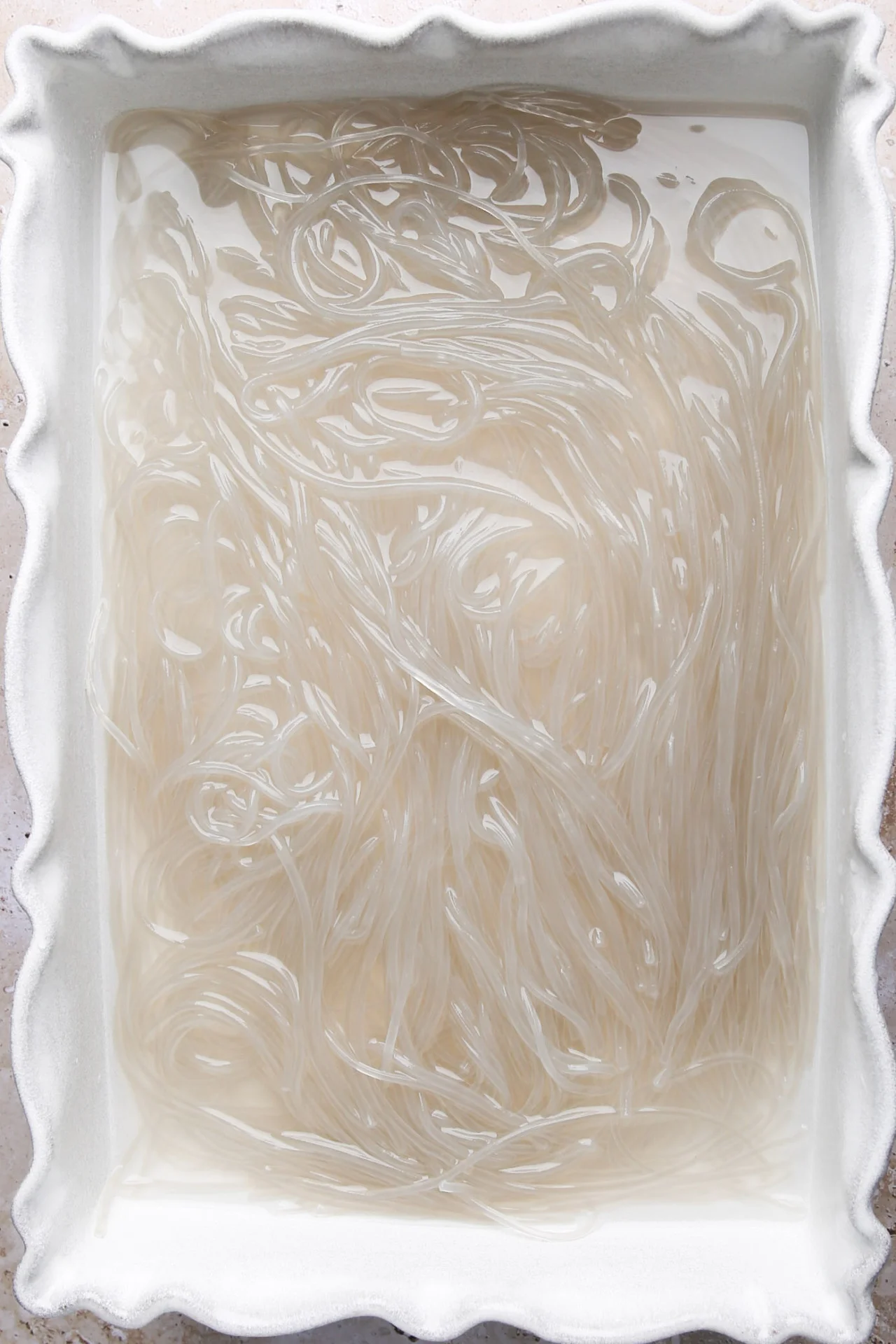 Fideos de cristal coreanos remoj&aacute;ndose en agua en un recipiente blanco