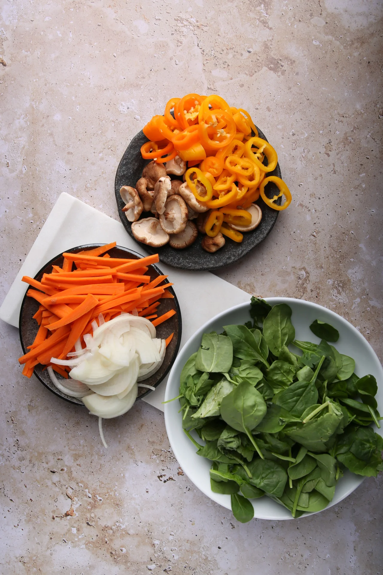 Ingredientes para japchae: pimientos en rebanadas, hongos, zanahorias, cebollas y espinacas frescas en platos