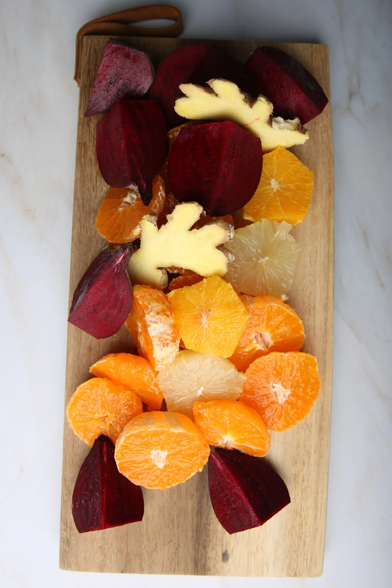 Tabla de cortar con betabel rebanado, naranjas peladas, gajos de toronja y un trozo de jengibre, listos para hacer jugo.