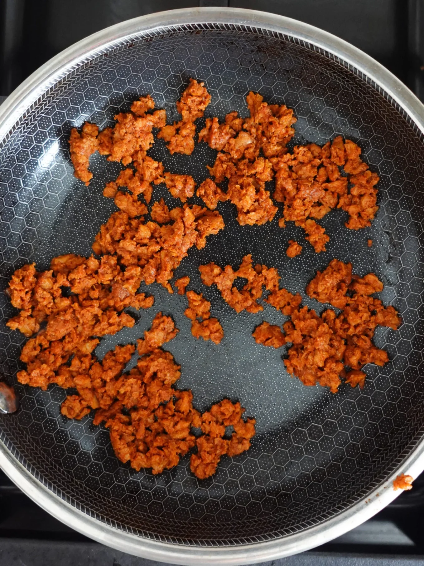 La carne picada cocida, dorada y desmenuzable -algo parecido al chorizo mexicano- se extiende irregularmente en una sartén antiadherente con forma hexagonal. La sartén se coloca sobre un hornillo, y el relleno queda perfecto para tacos o una torta de chorizo.