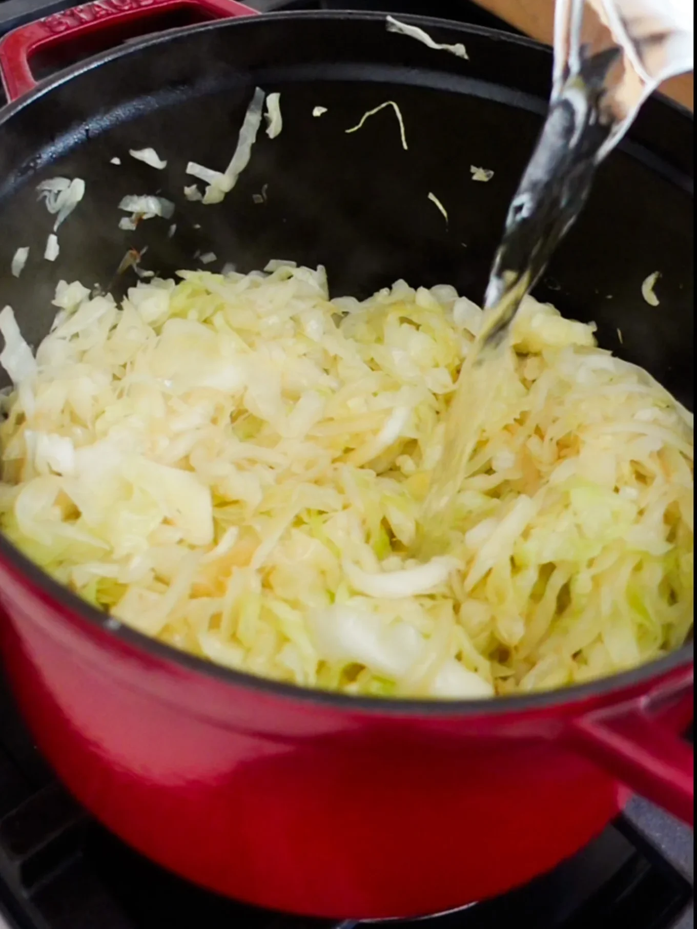 Col rebanada cocinándose en una olla roja sobre la estufa, con agua vertiéndose y vapor saliendo