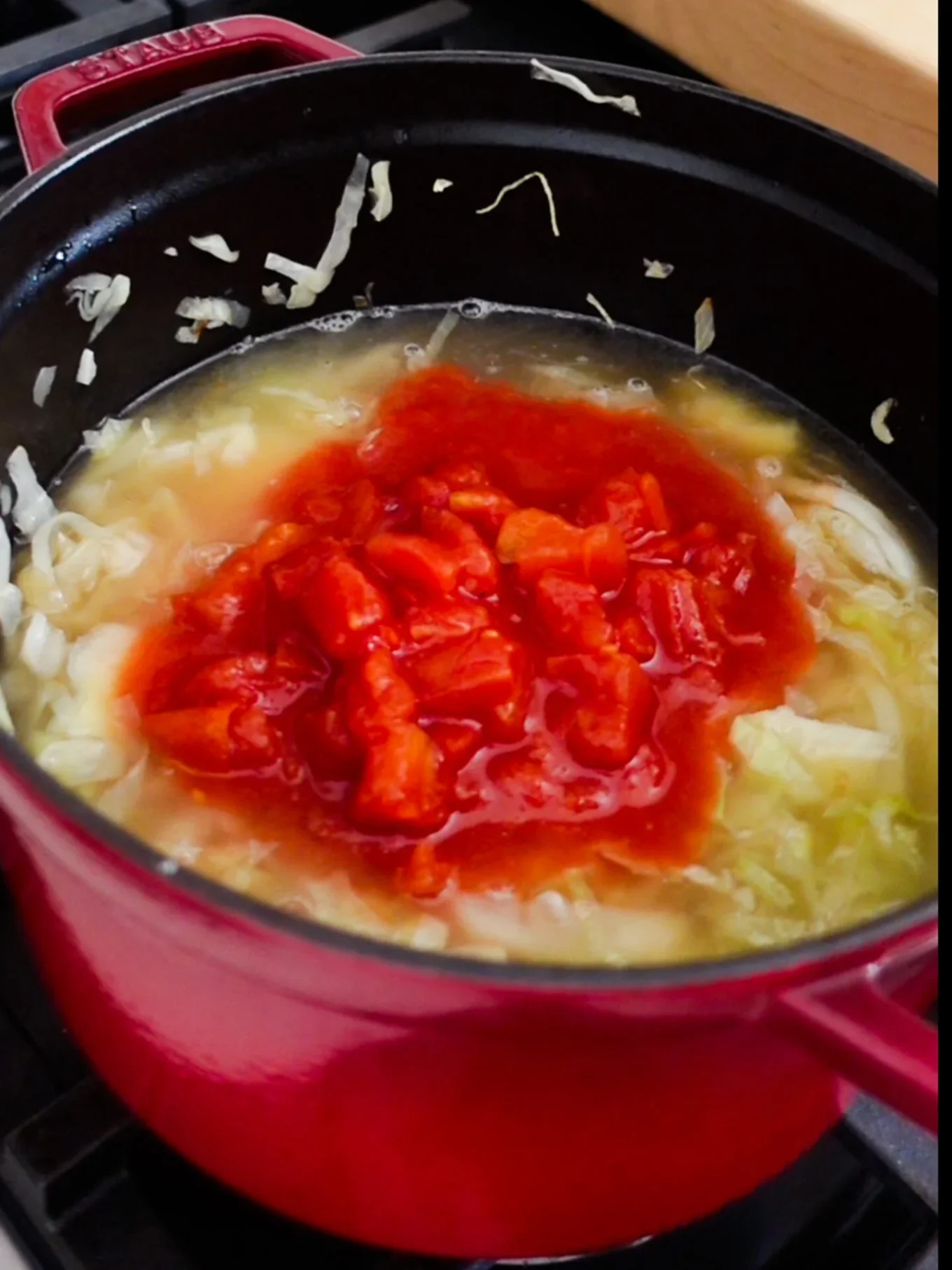 Olla roja sobre la estufa con col picada, caldo y tomate en cubitos cocinándose juntos para sopa de col mexicana